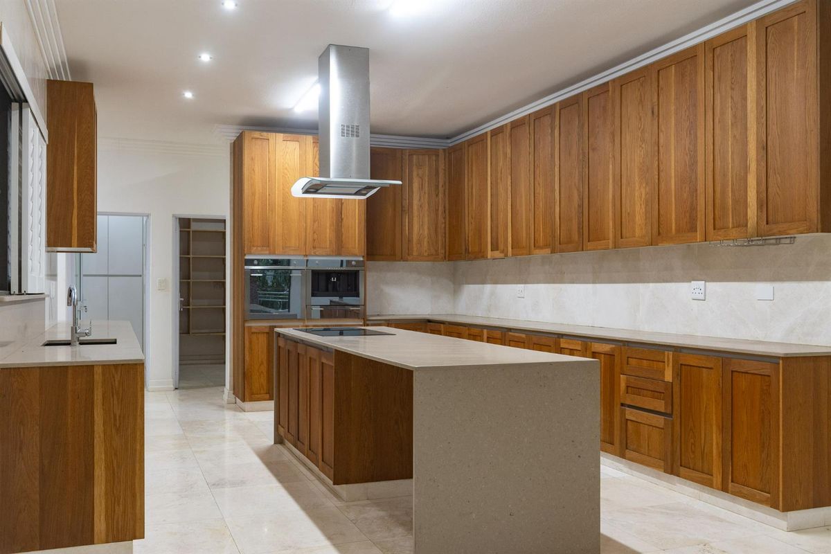 Spacious kitchen featuring warm timber cabinetry, stone countertops, a central island with integrated cooktop, and a stainless steel extractor fan.