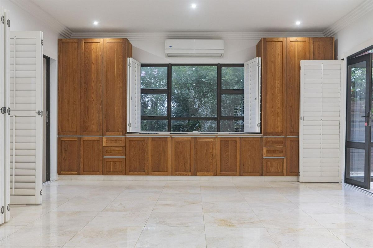 Spacious living area featuring extensive built-in wooden cabinetry, tiled flooring, plantation shutters, and a wall-mounted air conditioning unit.