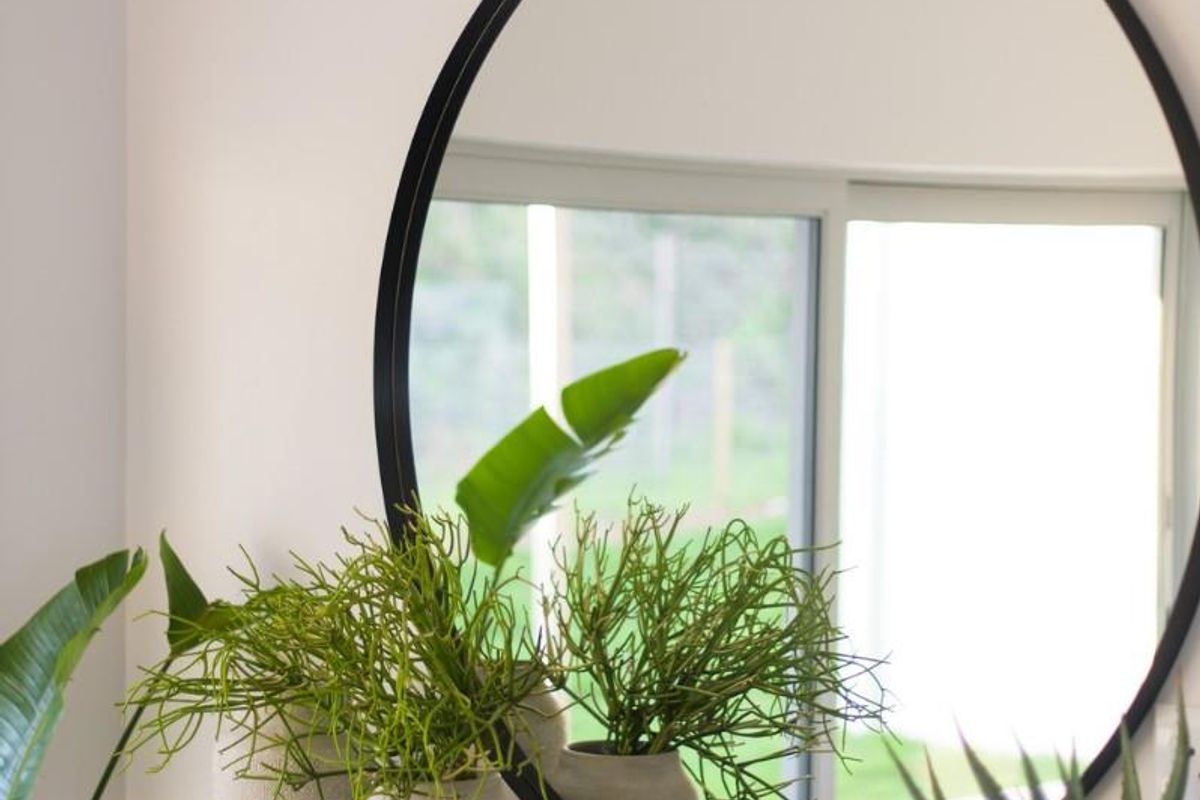 A bright interior space featuring a modern circular wall mirror and a sleek black console shelf, with views of the garden through sliding doors.