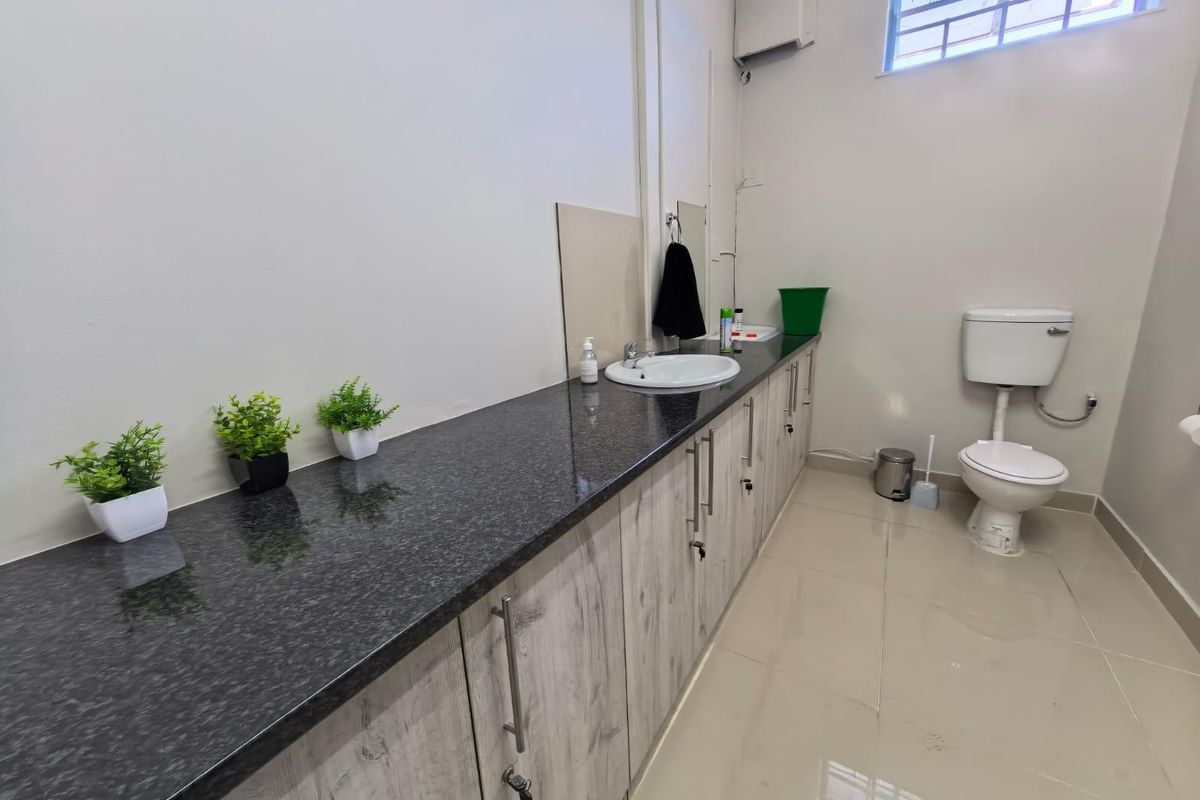 A functional commercial bathroom featuring a long granite countertop with an integrated basin, wood-look cabinetry, and a standard toilet.
