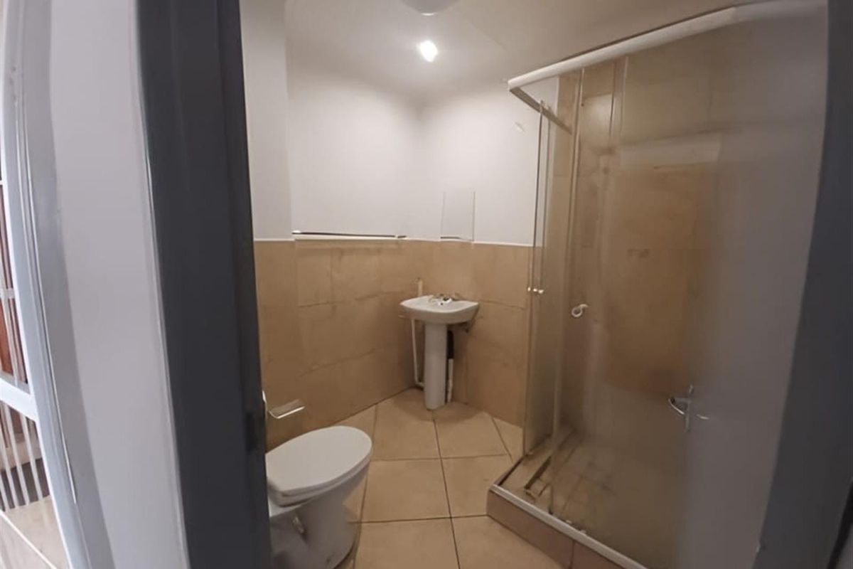 A functional bathroom featuring a pedestal sink, a toilet, and a glass-enclosed shower with neutral wall and floor tiling.