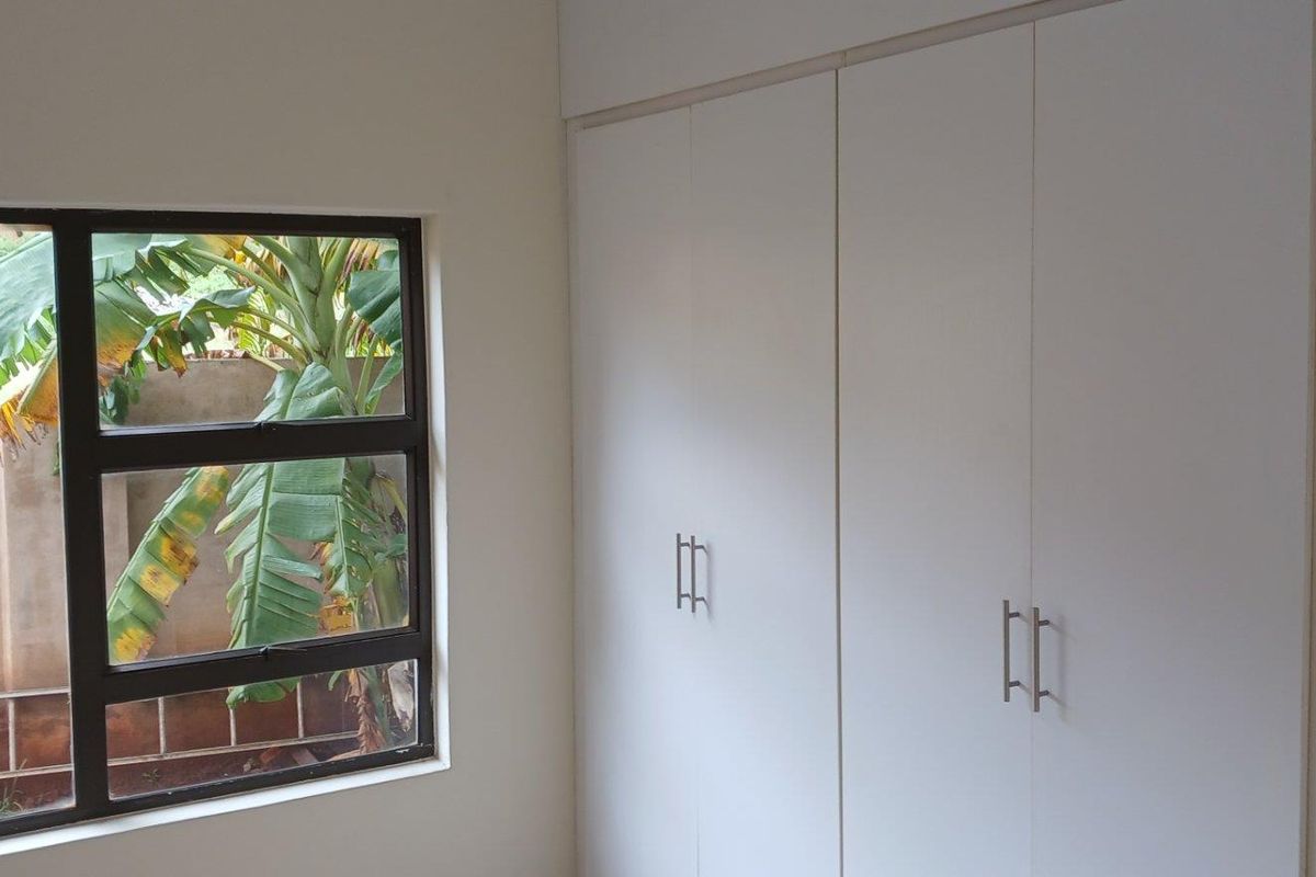 A bright bedroom featuring built-in white cabinetry and a window overlooking the garden area.