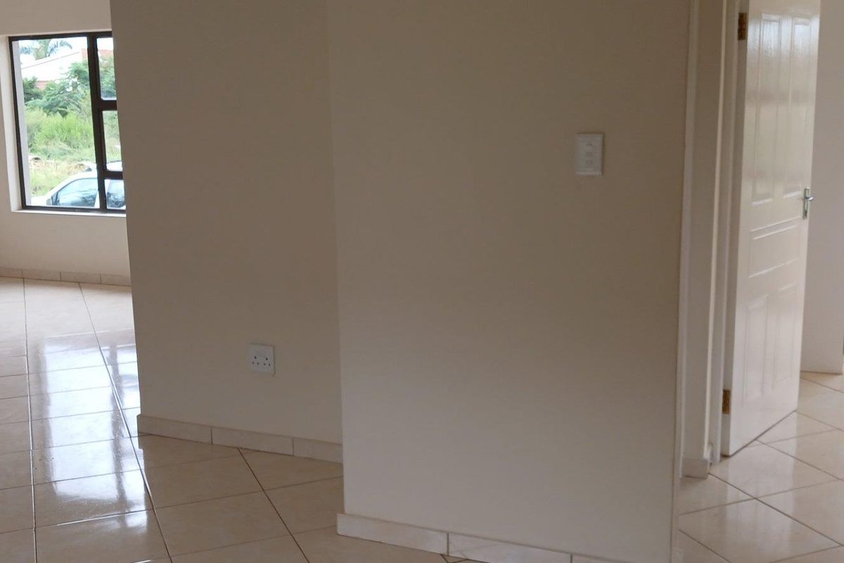 An empty interior living space featuring neutral tiled flooring, white walls, and multiple doorways leading to adjacent rooms.