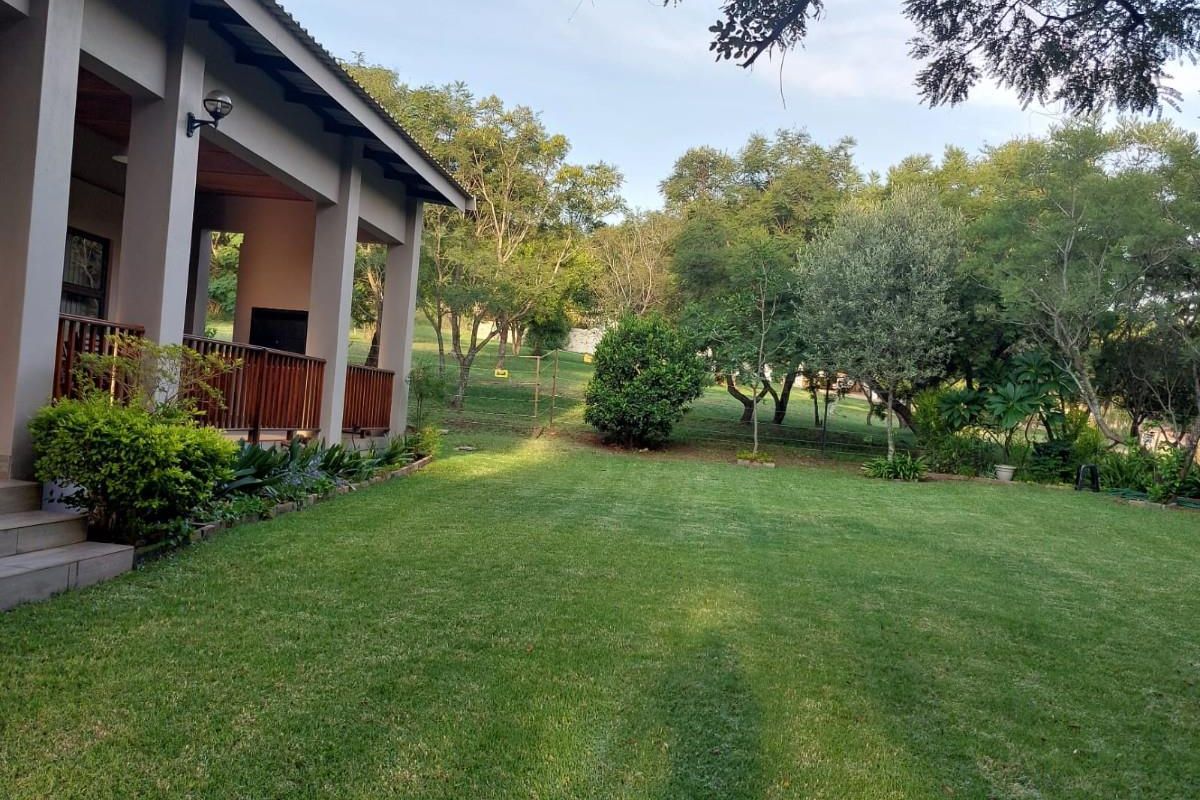A view of the rear garden featuring a well-maintained lawn, mature trees, and a covered patio area attached to the main house structure.