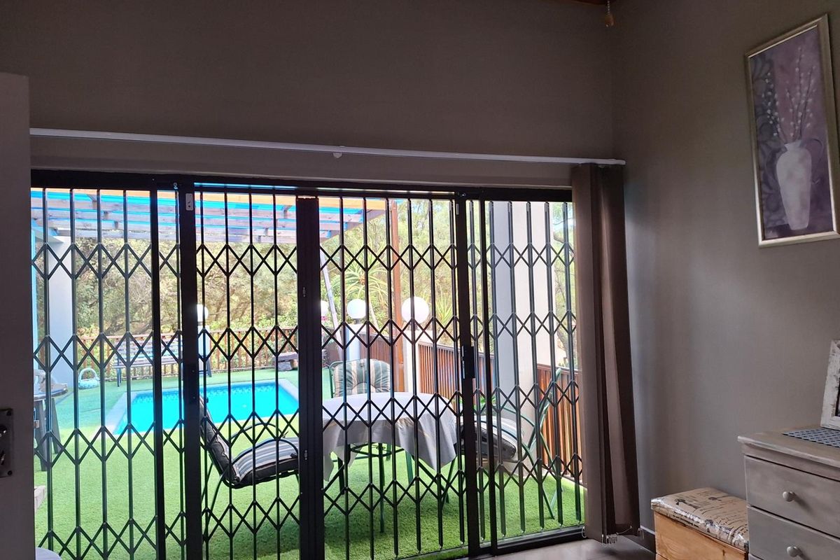 Living area featuring large sliding glass doors with security gates, providing direct access to an outdoor patio and swimming pool area.