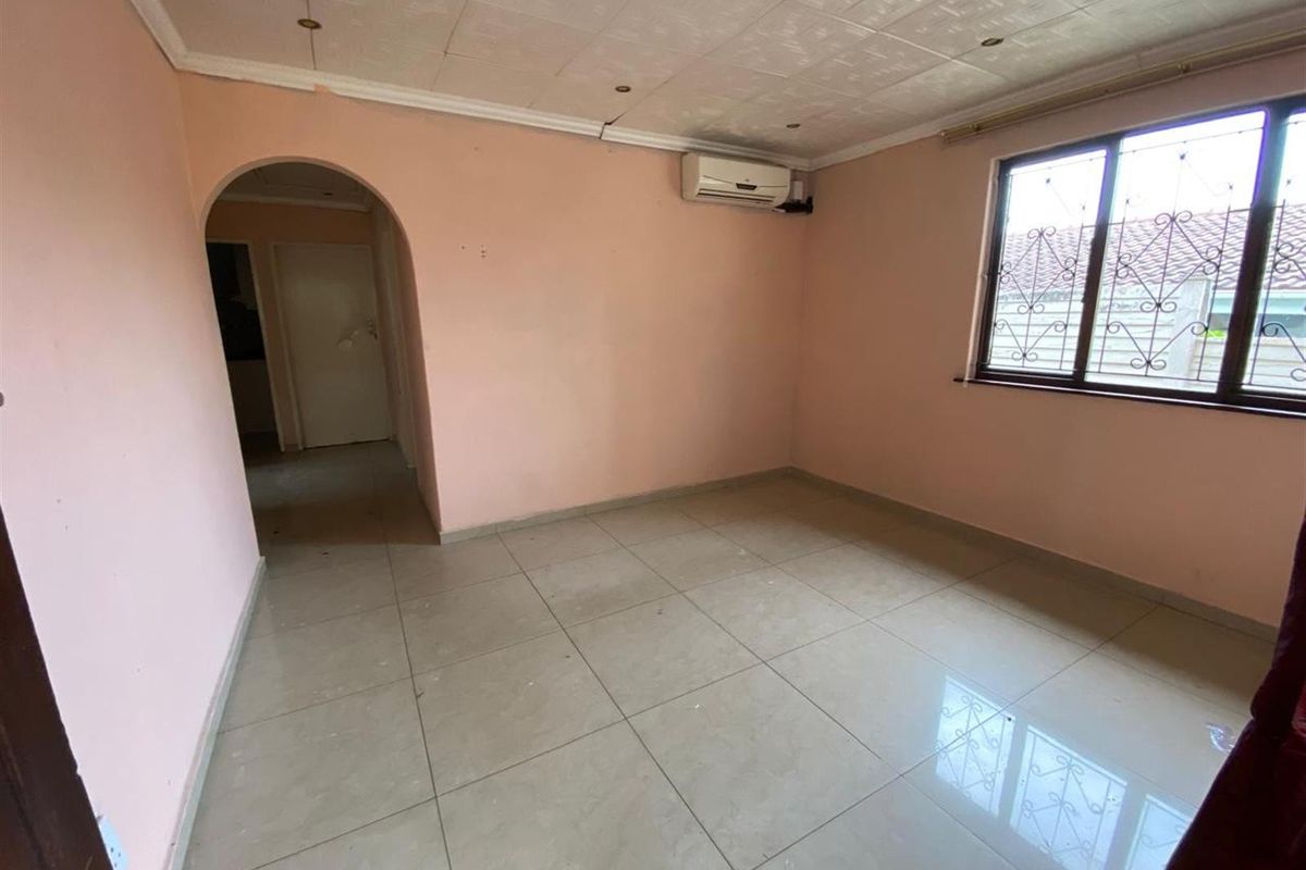 An empty living room featuring tiled flooring, an arched doorway, and a wall-mounted air conditioning unit.