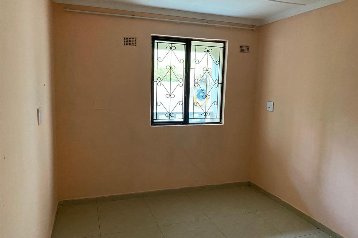 A vacant bedroom featuring tiled flooring, peach-toned walls, and a window fitted with decorative security burglar bars.