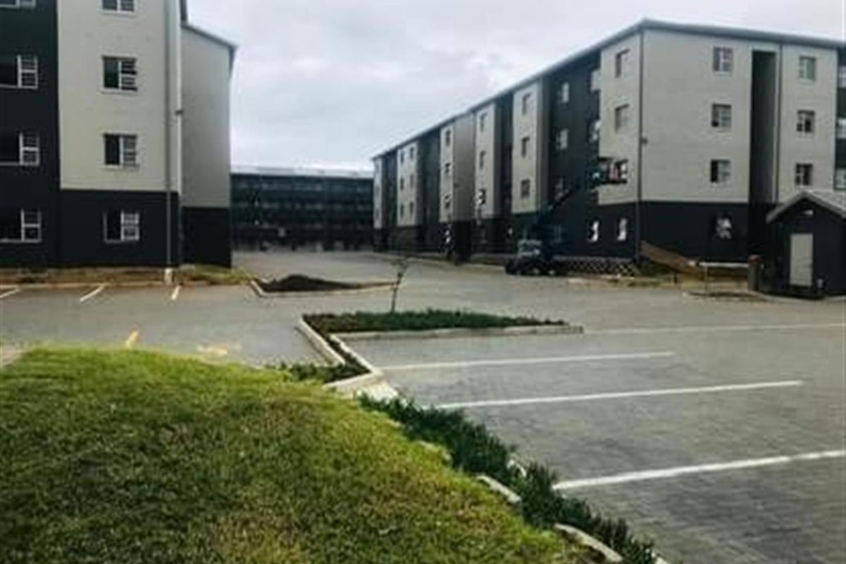 Exterior view of a modern apartment complex featuring paved parking areas, landscaped grass verges, and multi-story residential buildings with a contemporary facade.