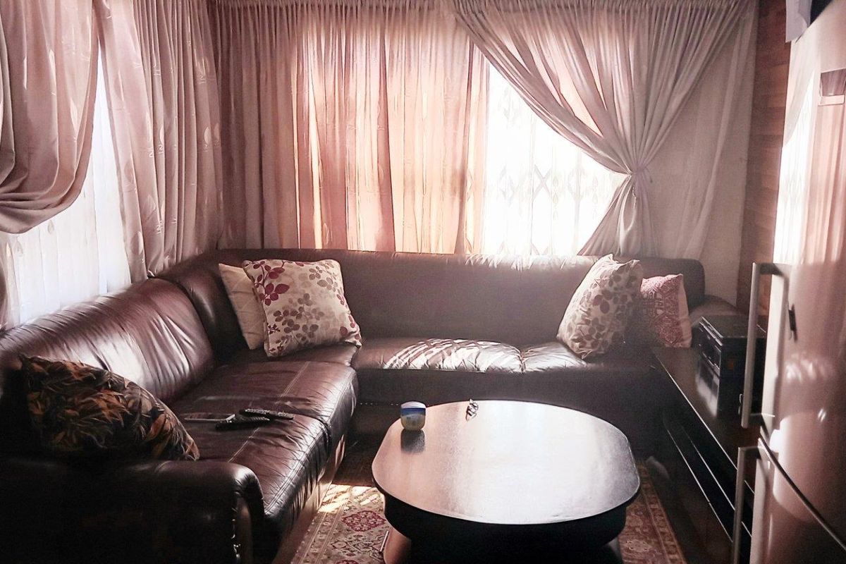 A cozy living room featuring large windows with curtains, providing natural light and a comfortable seating area.