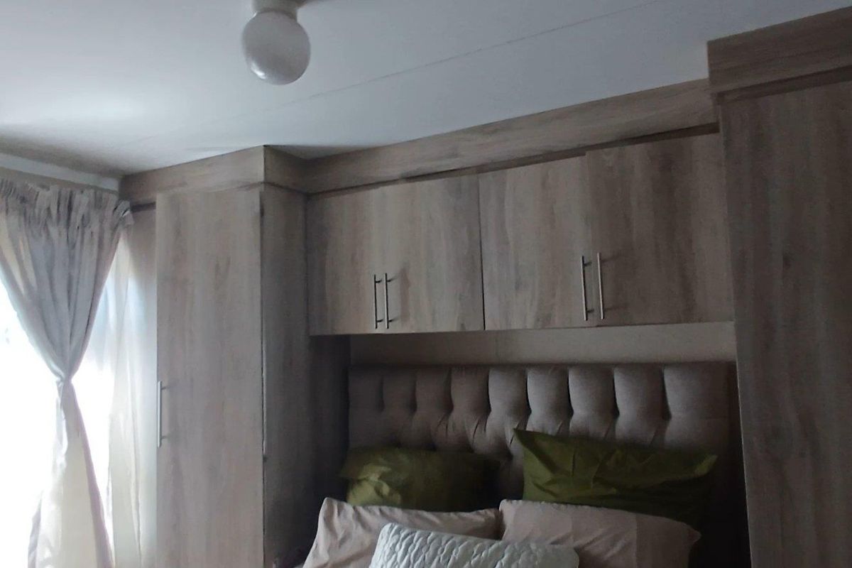 A bedroom featuring built-in wooden cabinetry and overhead storage units surrounding the bed area.