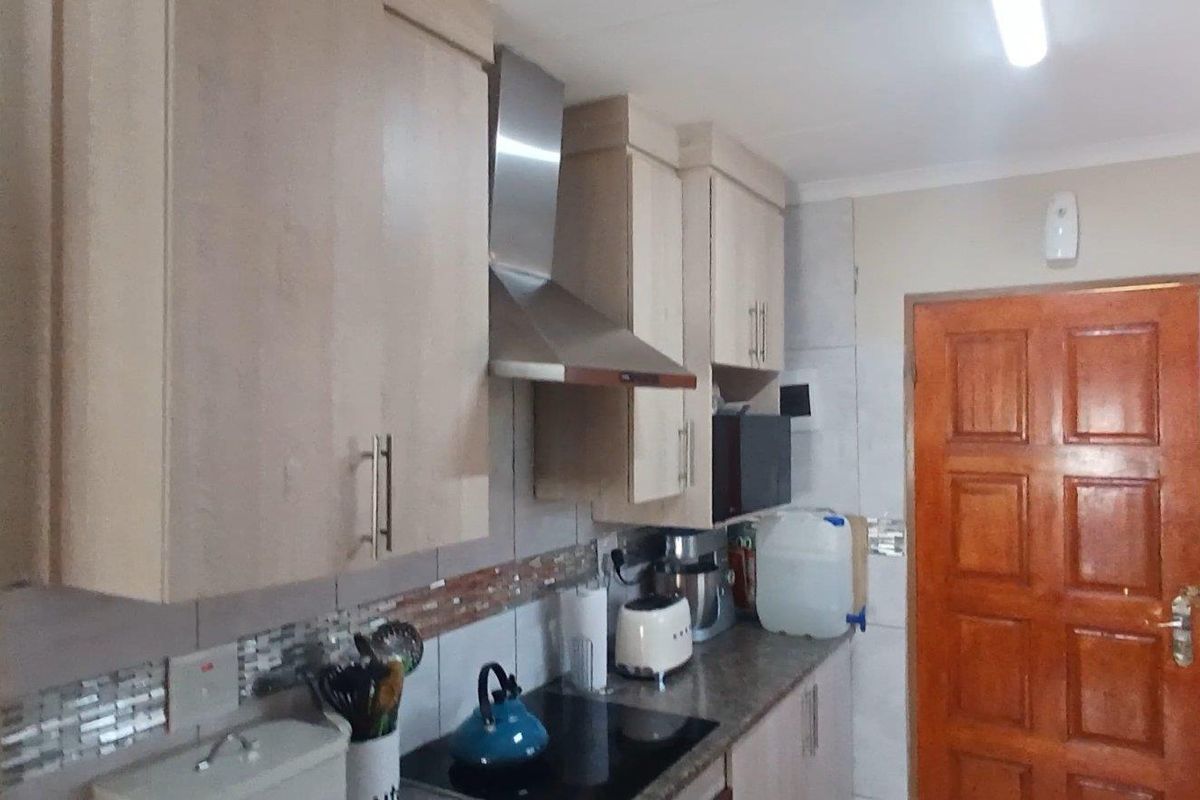 A functional kitchen featuring light wood cabinetry, a stainless steel extractor fan, a built-in hob, and tiled splashbacks.