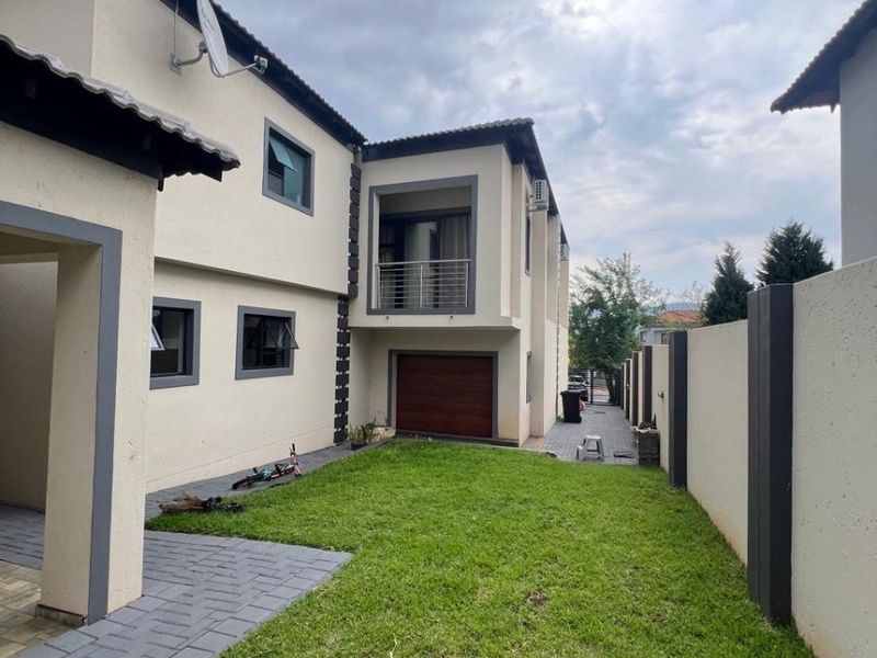 Rear view of the property featuring a landscaped garden, paved walkway, balcony, and integrated garage access.