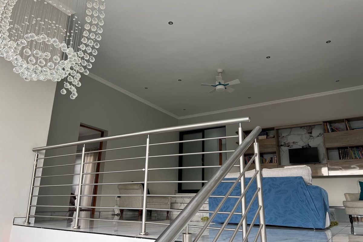 Spacious living area featuring a modern stainless steel balustrade, recessed lighting, ceiling fan, and integrated built-in shelving unit.