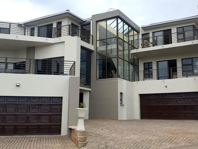Modern multi-level residential property featuring a double garage, expansive glass facade, and multiple balconies with metal railings.