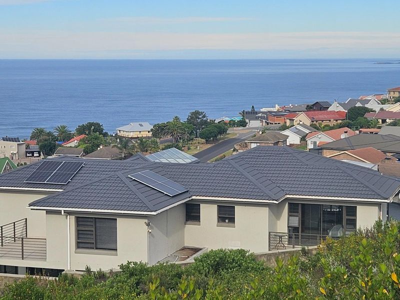 An elevated view of a residential property featuring a tiled roof with solar panels, a balcony, and scenic coastal views.
