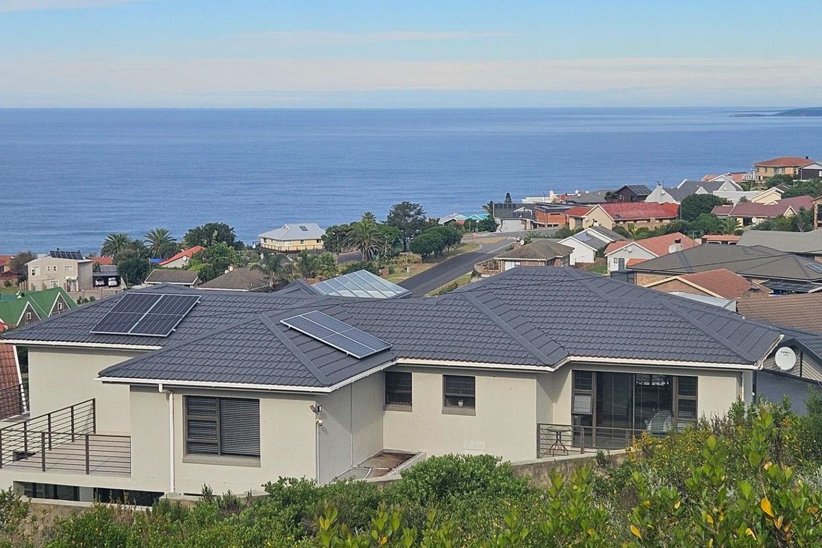 An elevated view of a residential property featuring a tiled roof with solar panels, a balcony, and scenic coastal views.