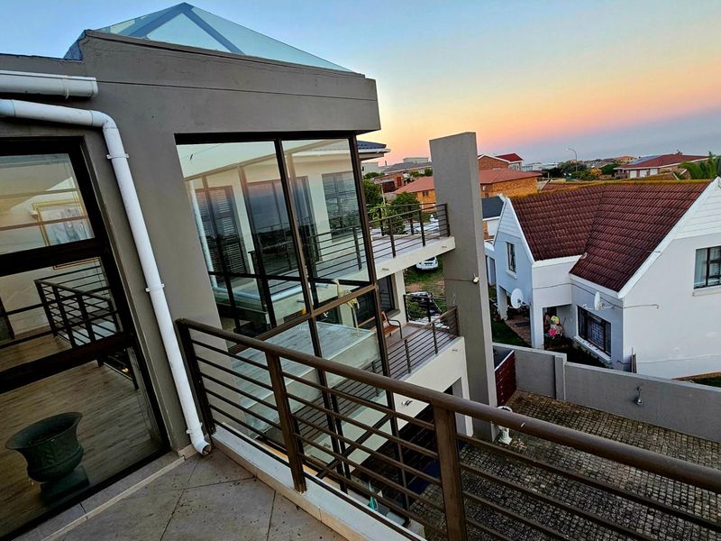 A modern elevated balcony featuring metal railings, tiled flooring, and a glass skylight, offering an expansive view of the surrounding residential neighborhood.