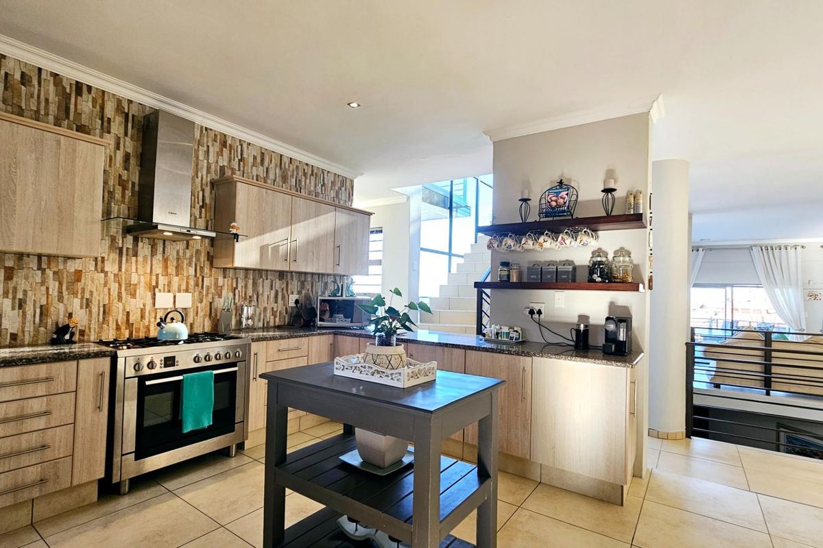 Modern kitchen featuring light wood cabinetry, stone feature wall, gas stove with extractor fan, and tiled flooring, seamlessly flowing into the adjacent living area.