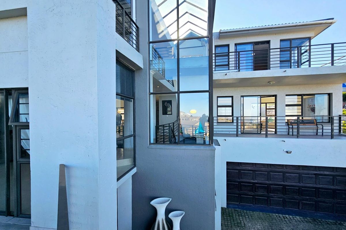 Modern multi-level rear exterior featuring a striking glass atrium, spacious balconies with metal railings, and an integrated double garage.