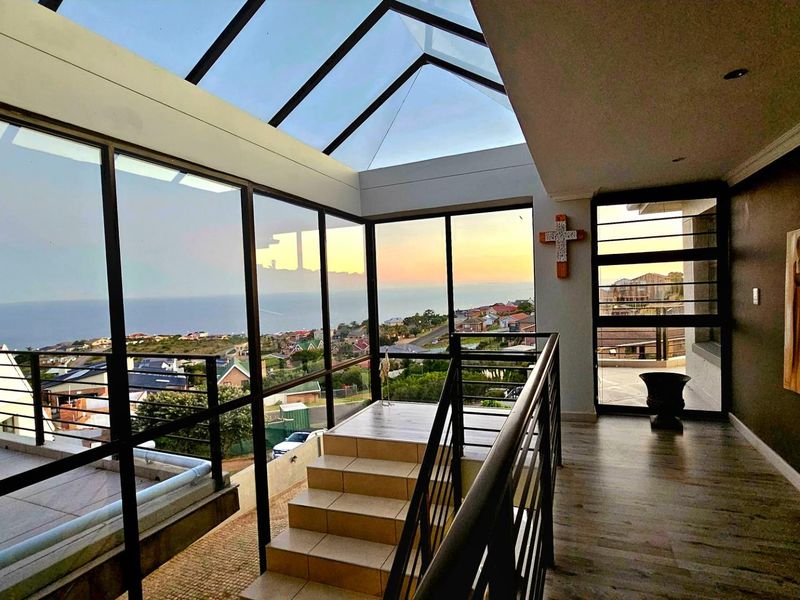 A modern, light-filled enclosed balcony or sunroom featuring a glass roof, expansive coastal views, and high-quality finishes.