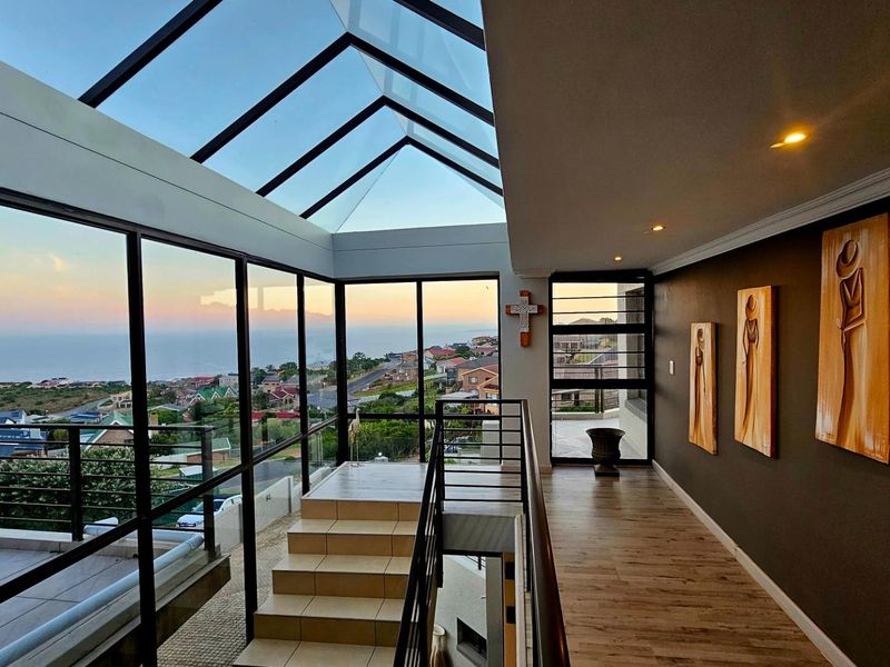 A bright, modern hallway featuring a large glass skylight, tiled staircase, and expansive windows offering panoramic coastal views.