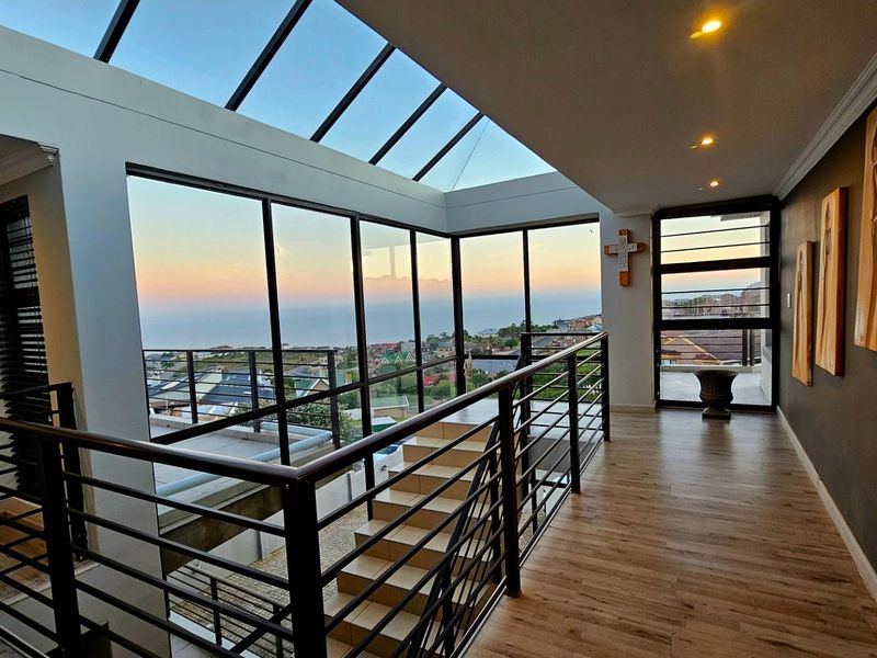 Spacious hallway featuring a striking glass roof, modern metal balustrades, and expansive windows offering panoramic coastal views.