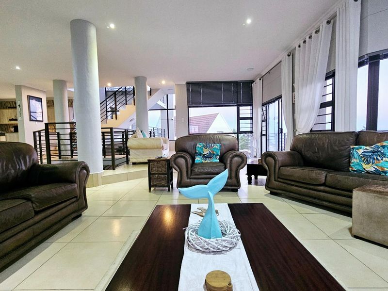Spacious open-plan living area featuring tiled floors, structural columns, and a staircase, with large windows providing ample natural light.