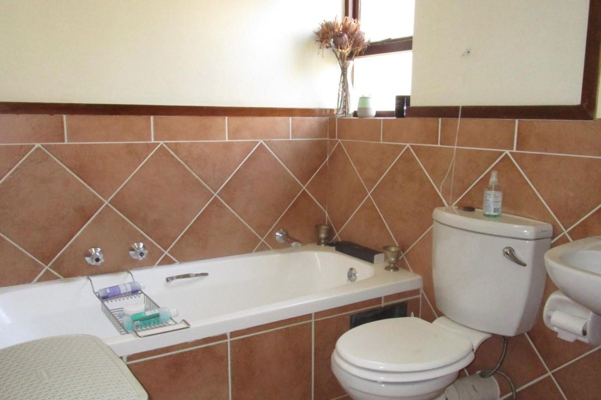 A functional bathroom featuring a built-in bathtub, pedestal basin, and toilet with classic brown tiled splashbacks.