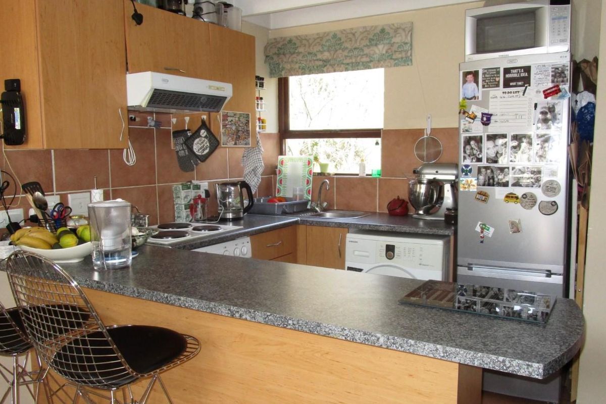A functional kitchen featuring laminate cabinetry, a breakfast bar, ceramic tile backsplash, and integrated appliances including an electric hob and extractor fan.
