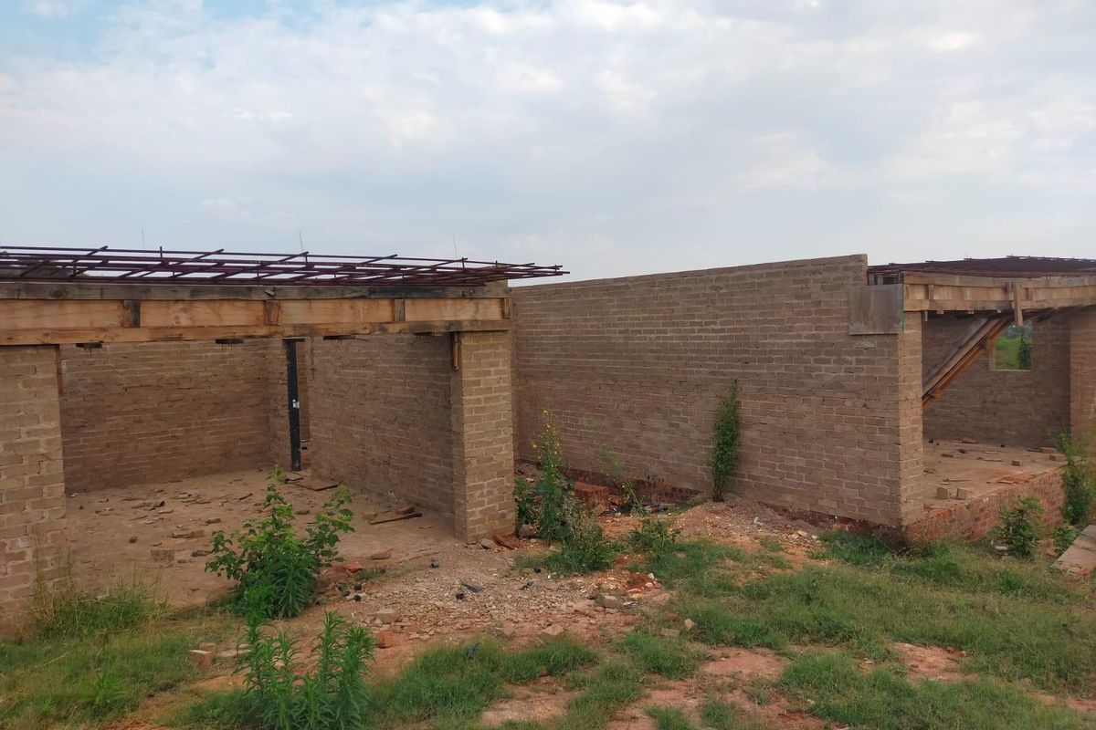 An unfinished residential structure showing exposed brick walls and timber roof framing, currently in the early stages of construction.