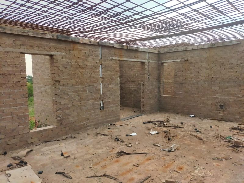 An unfinished construction site showing exposed brick walls and a steel rebar roof structure, requiring significant completion and finishing work.