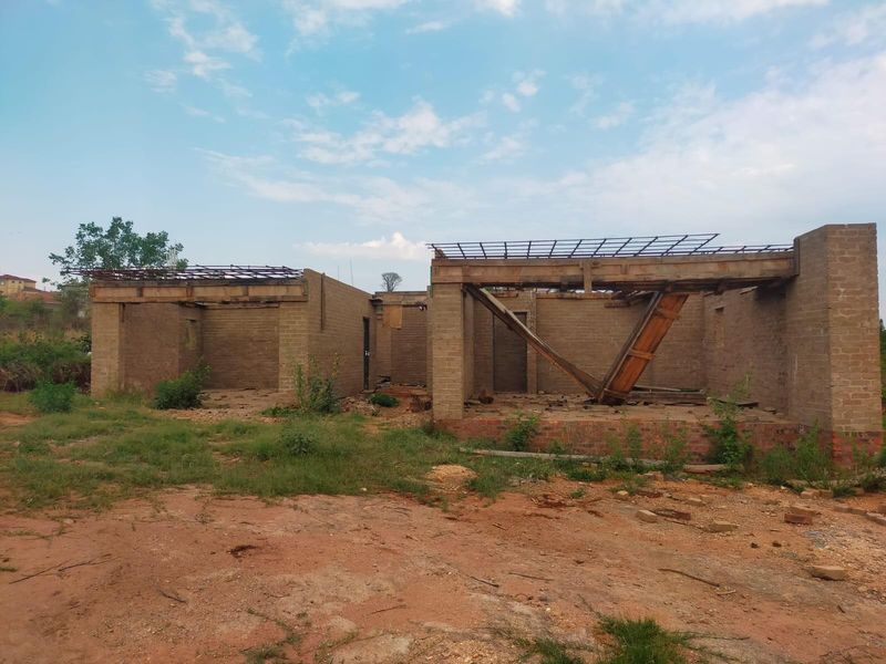 An unfinished residential structure showing exposed brick walls and roof trusses, currently in a shell state requiring significant completion.