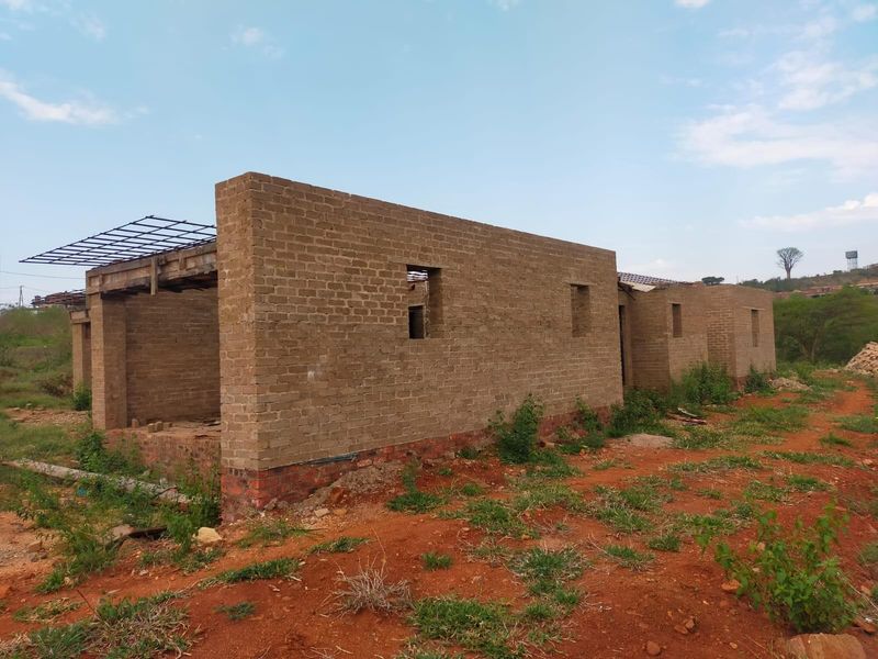 An unfinished residential structure showing exposed brick walls and roof framing, currently in the early stages of construction.