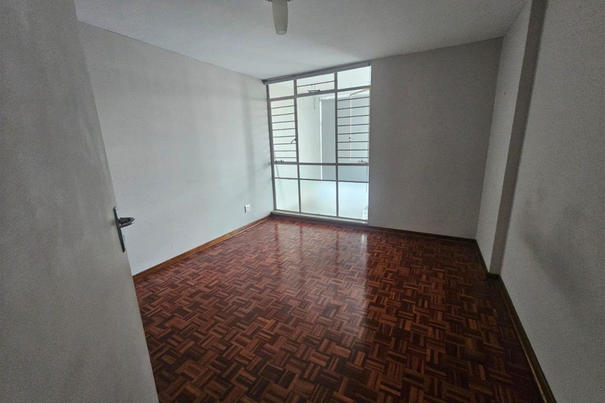 An empty bedroom featuring classic parquet flooring and a large window that allows for natural light.