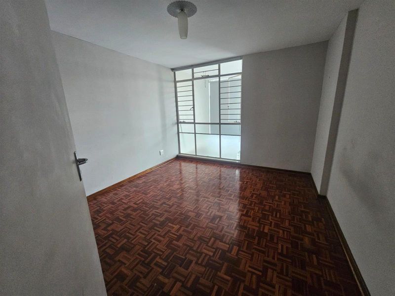An empty bedroom featuring classic parquet flooring and a large window that allows for natural light.