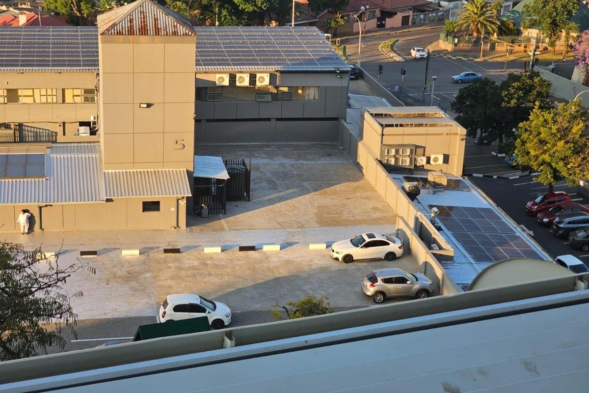 Aerial view of the apartment complex exterior, featuring a paved parking area, rooftop solar panels, and external air conditioning units.