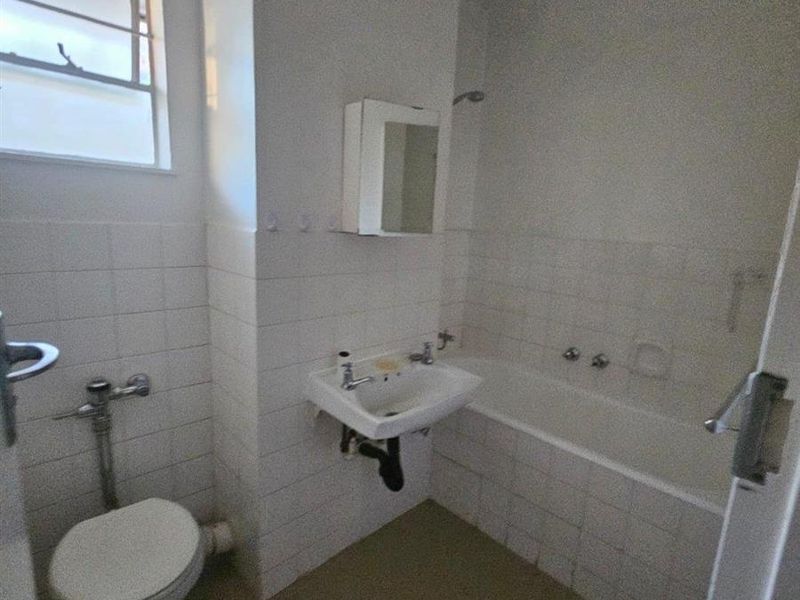 A functional bathroom featuring a bathtub, wall-mounted basin, and toilet, with classic white wall tiling and a louvered window for ventilation.