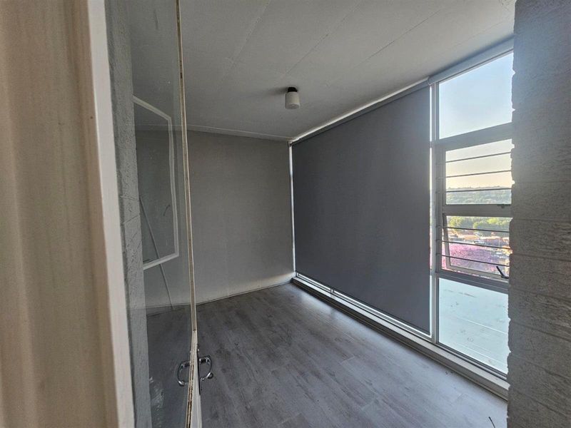 A bright, empty bedroom featuring modern laminate flooring, large windows with roller blinds, and a neutral color palette, ready for personalization.