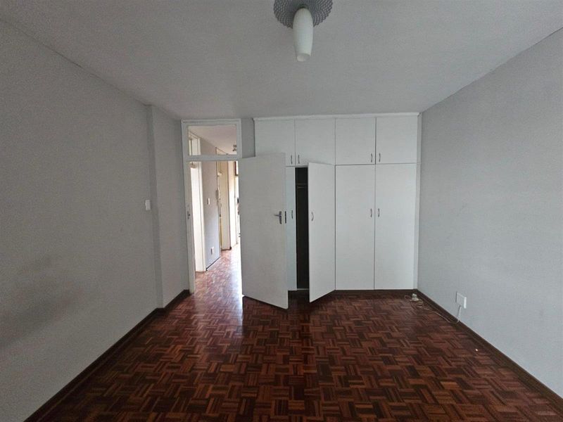 An empty bedroom featuring classic parquet flooring and white built-in cupboards with overhead storage.
