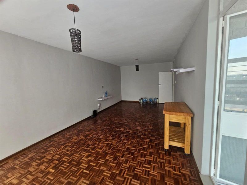 Spacious living area featuring classic parquet flooring, neutral wall tones, and minimalist wall-mounted shelving, offering a versatile blank canvas for interior design.