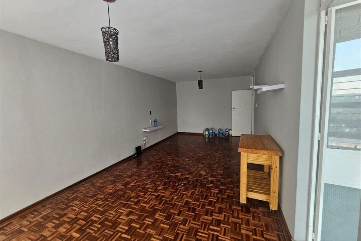 Spacious living area featuring classic parquet flooring, neutral wall tones, and minimalist wall-mounted shelving, offering a versatile blank canvas for interior design.