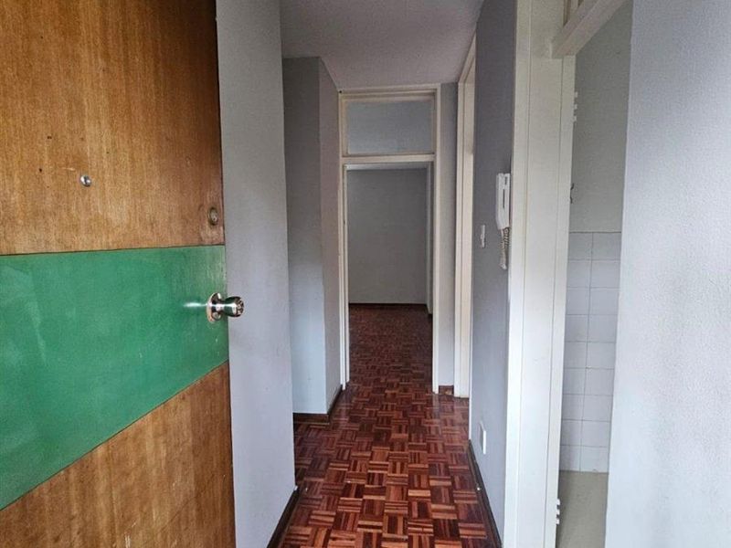 A functional hallway featuring classic parquet flooring, an intercom system, and transom windows above the doorways, providing access to various rooms in the apartment.