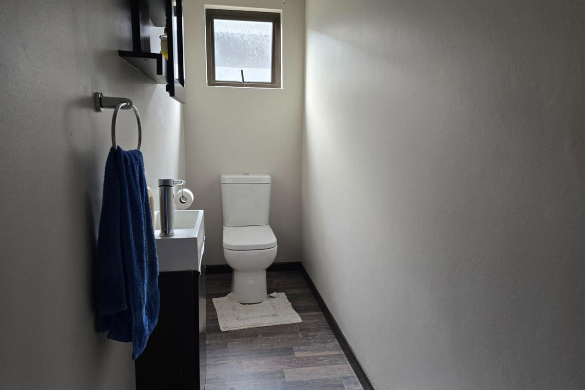 A compact guest bathroom featuring a modern vanity, toilet, and wood-look flooring with a small window for natural light.