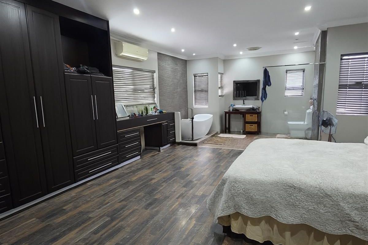 Spacious bedroom featuring integrated dark wood cabinetry, an open-plan en-suite bathroom with a freestanding bathtub, and modern wood-look flooring.