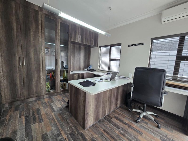 A functional home office featuring extensive built-in dark wood cabinetry, a matching integrated desk, laminate flooring, and a wall-mounted air conditioning unit.