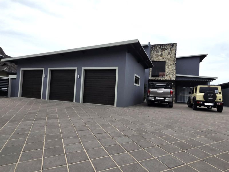 Modern residential exterior featuring a triple garage, stone cladding accents, and a spacious paved driveway.