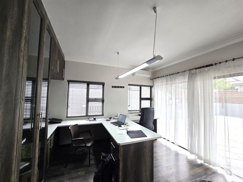 A well-appointed home office featuring extensive built-in cabinetry, a spacious desk, laminate flooring, and direct access to the patio through sliding glass doors.