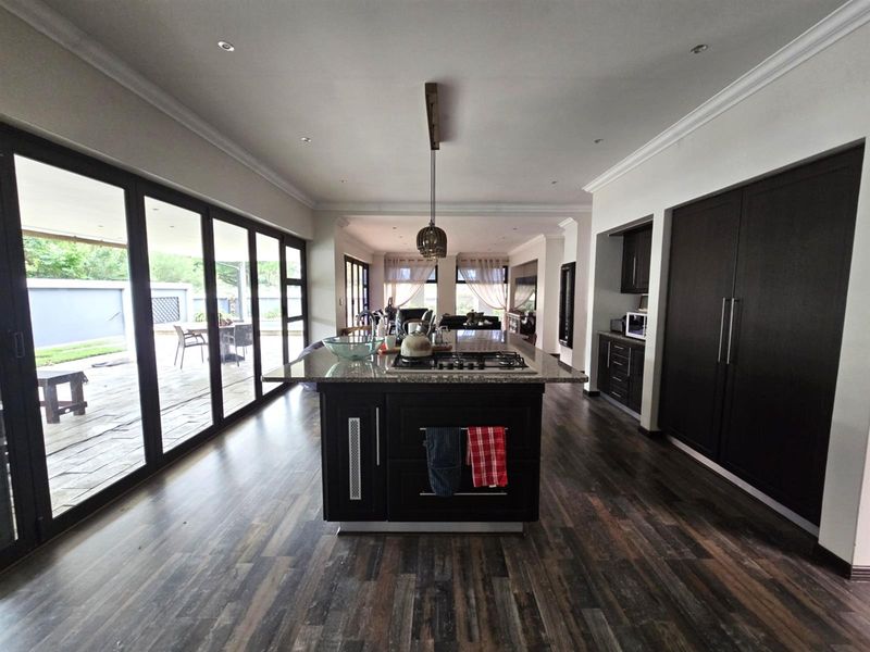 Spacious open-plan kitchen and living area featuring a central island with gas hob, dark cabinetry, granite countertops, and large sliding doors leading to the patio.