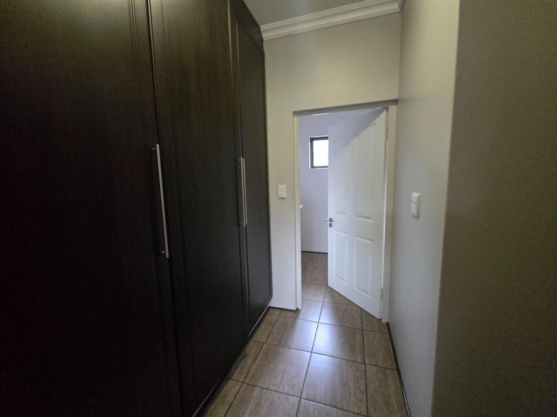 A clean hallway featuring dark wood built-in cupboards and neutral tiled flooring, leading through to an adjacent room.