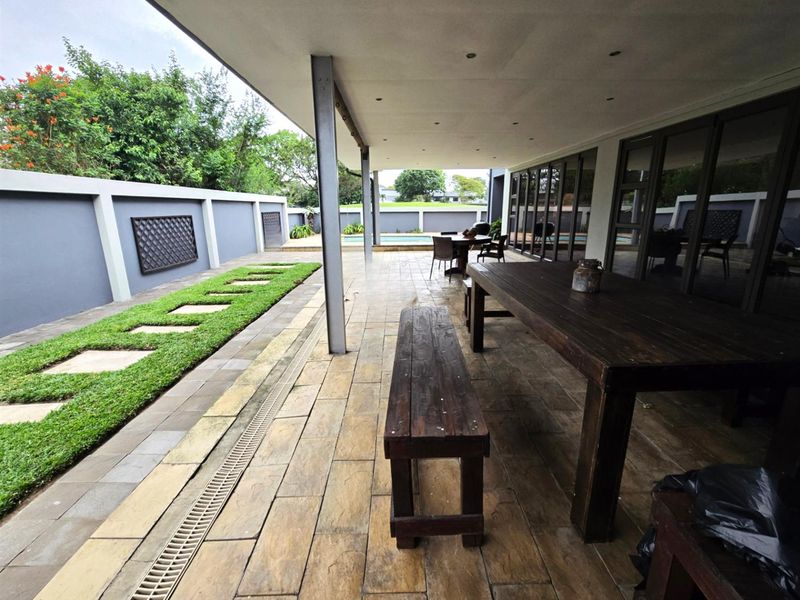 Spacious covered patio featuring stone-look tiling, recessed lighting, and direct access to the garden and pool area through large sliding glass doors.